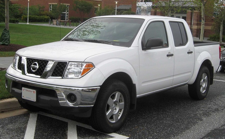 An older Nissan Frontier with a white paint job sits parked on the street.