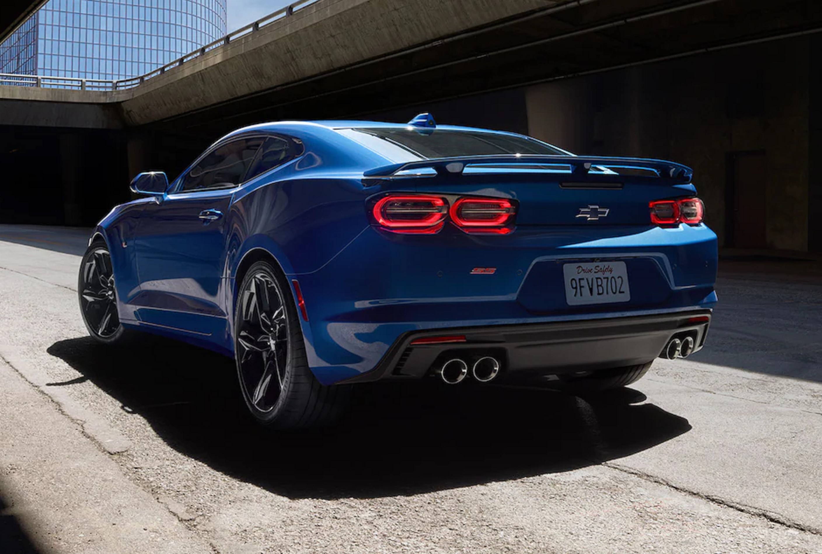 The rear 3/4 view of a blue 2022 Chevrolet Camaro SS on a city street below a bridge