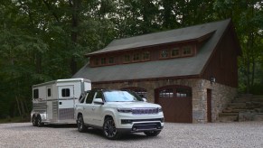 Promo photo of a Jeep Grand Wagoneer full-size SUV with a horse trailer parked in front of a barn.