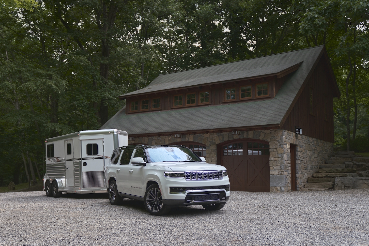 Promo photo of a Jeep Grand Wagoneer full-size SUV with a horse trailer parked in front of a barn.