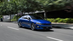 A blue 2022 Kia K5 driving down a tree-lined city street