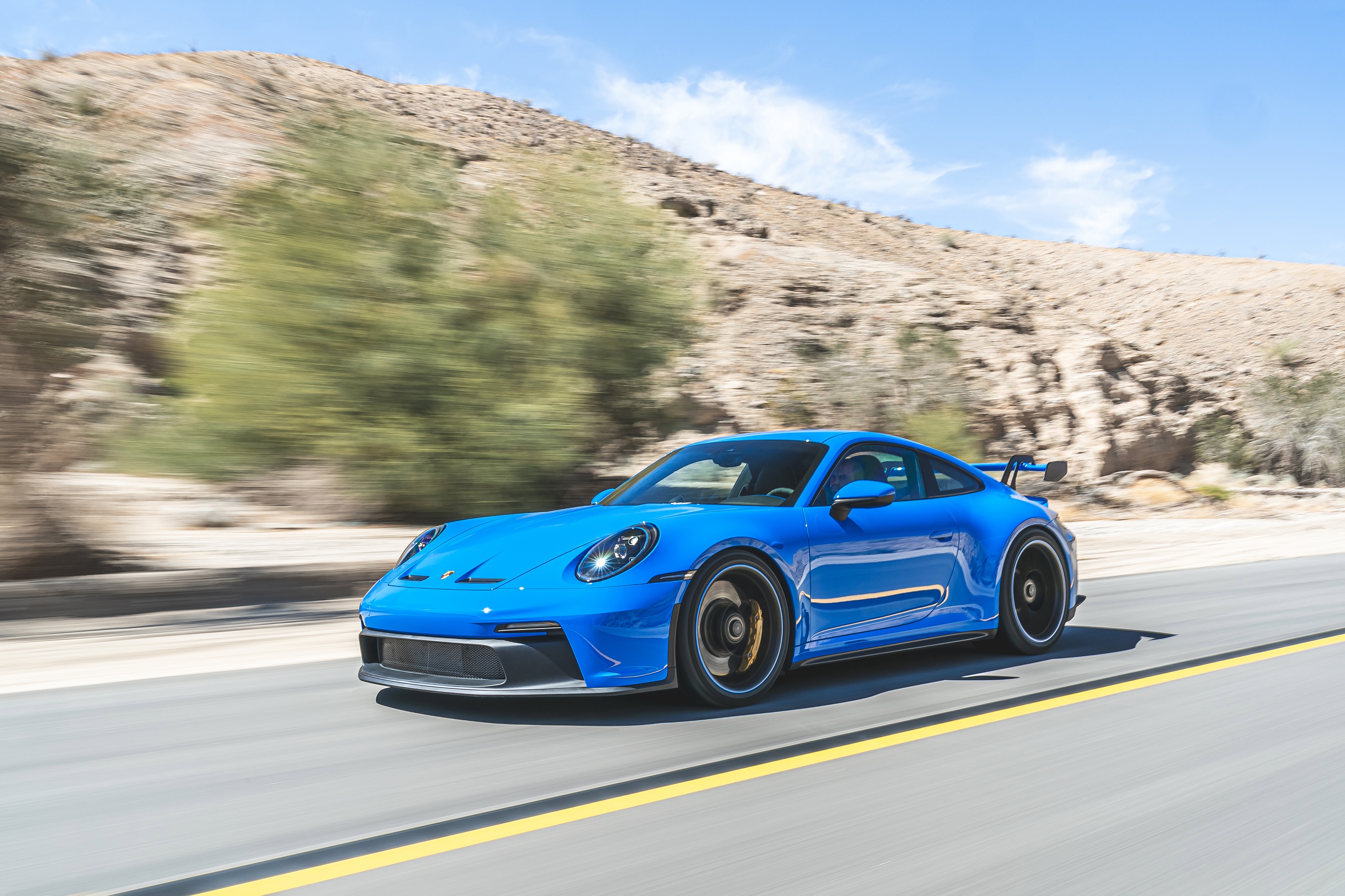 A blue 2022 Porsche 911 GT3 driving down a desert canyon road