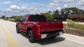 Red Toyota Tundra 4x4 pickup truck driving away down a country road, a train visible in the background.