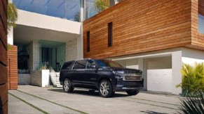 A dark colored Chevy Suburban outside of a house.