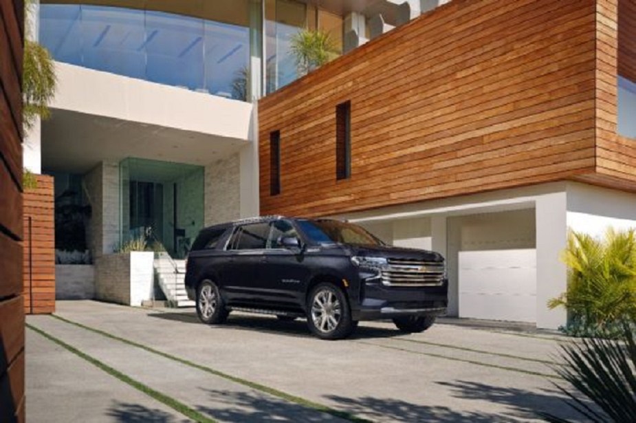 A dark colored Chevy Suburban outside of a house. 