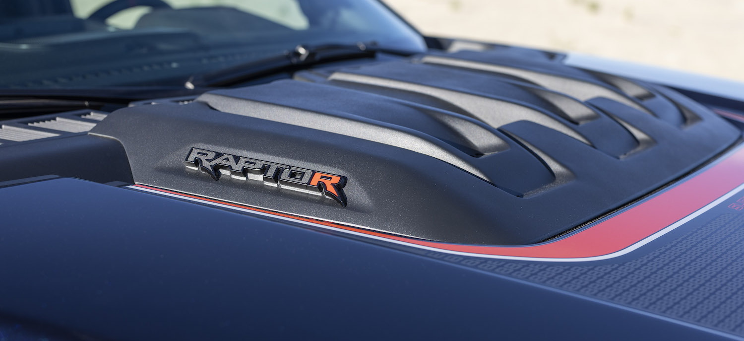 Closeup of the badges on the hood scoop of an F-150 Raptor R above its V8 engine.