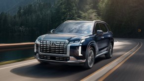 A blue 2023 Hyundai Palisade midsize SUV is driving on the road.