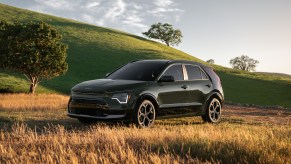 A dark color 2023 Kia Niro parked in a field and mountainous area.