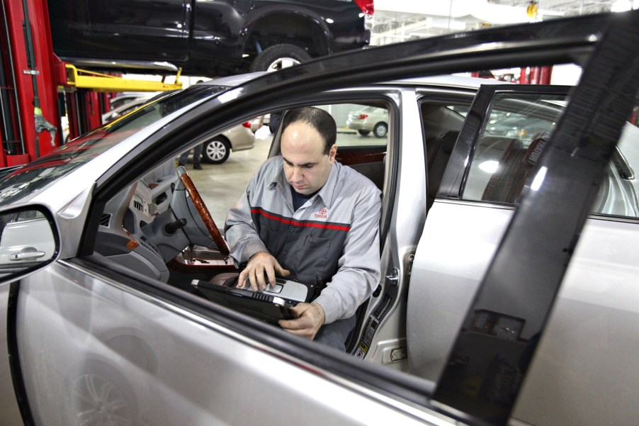 A gray-clothed car mechanic uses an OBD2 scanner to check for diagnostic trouble codes in a silver Toyota Avalon