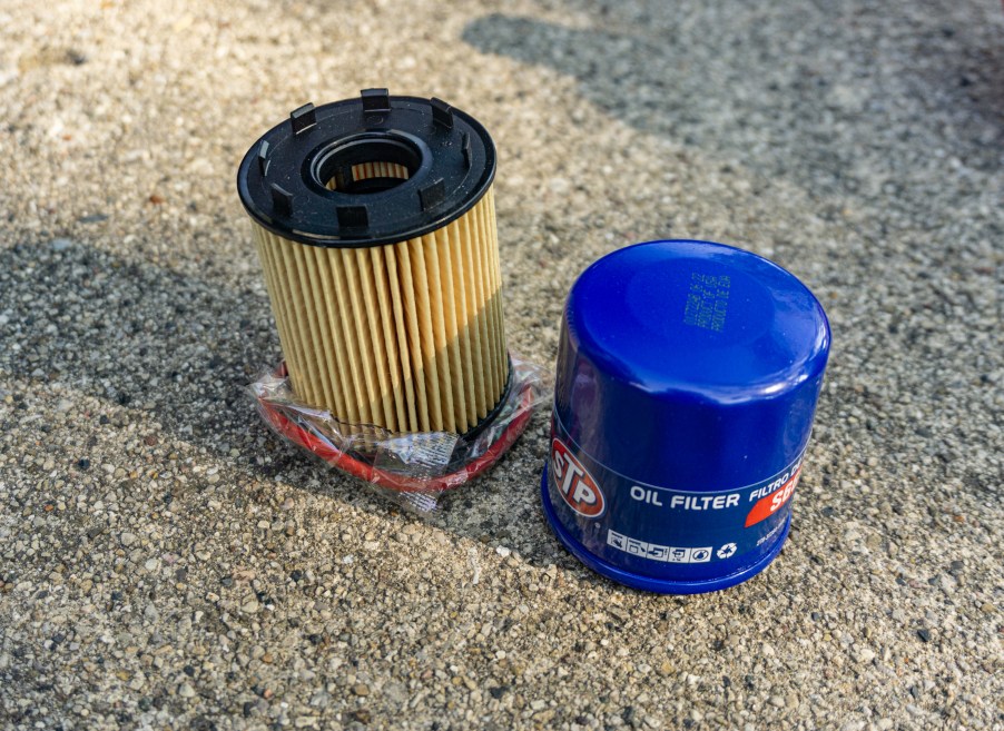 A yellow cartridge oil filter next to a blue spin-on oil filter on the ground