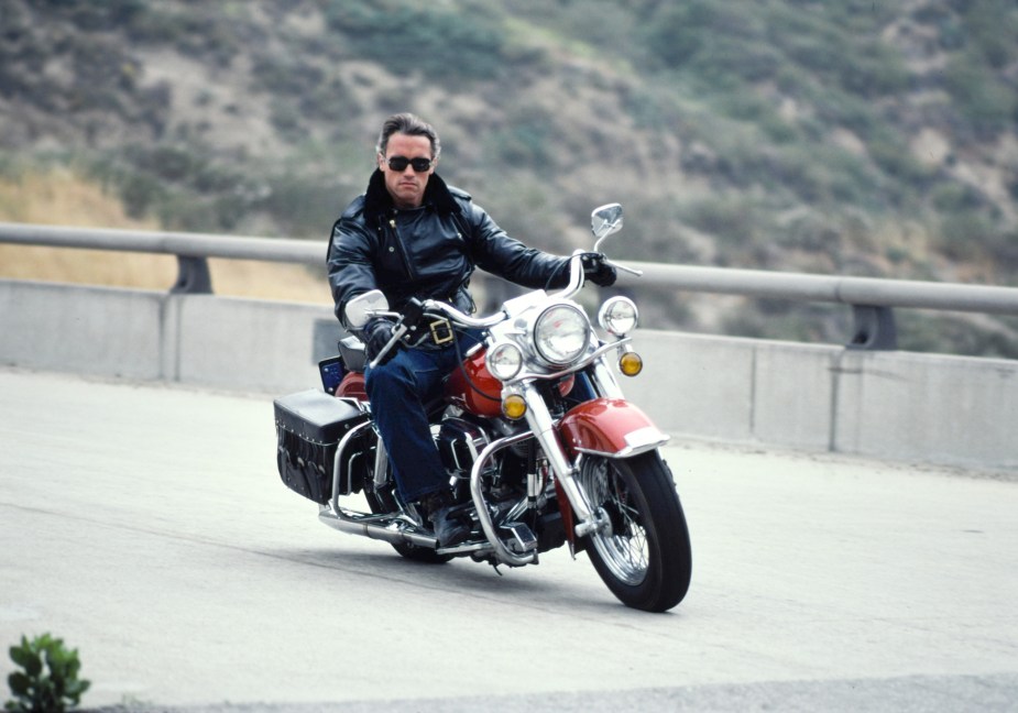 Arnold Schwarzenegger going around a corner faster on a motorcycle. 