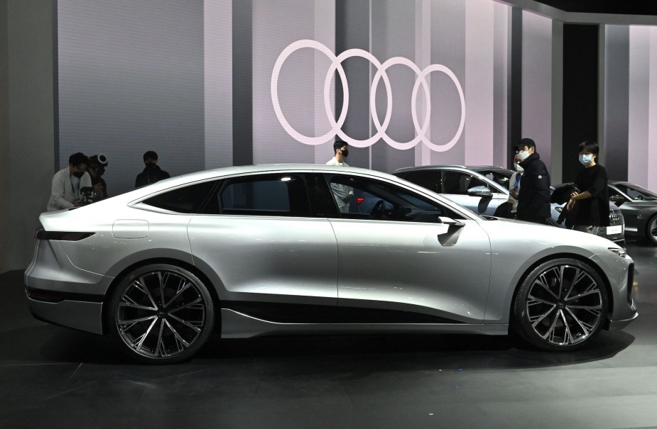 A silver Audi A6 e-tron parked indoors in front of the Audi logo. 