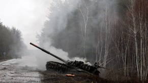 Russian tank burning by the side of a Ukrainian road, birch trees visible in the background.