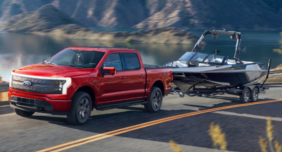 A red 2022 Ford F-150 Lightning is towing a boat.