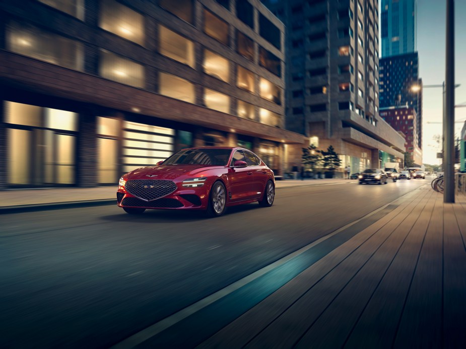 A red 2023 Genesis G70 driving down a city street at night