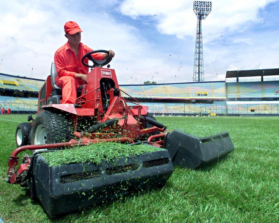 A lawn mower mowing grass that needs clearing up clumped grass. 