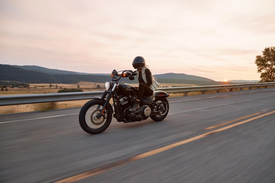 A woman riding a harley-davidson motorcycle down an open road in the middle of a daytime desert.