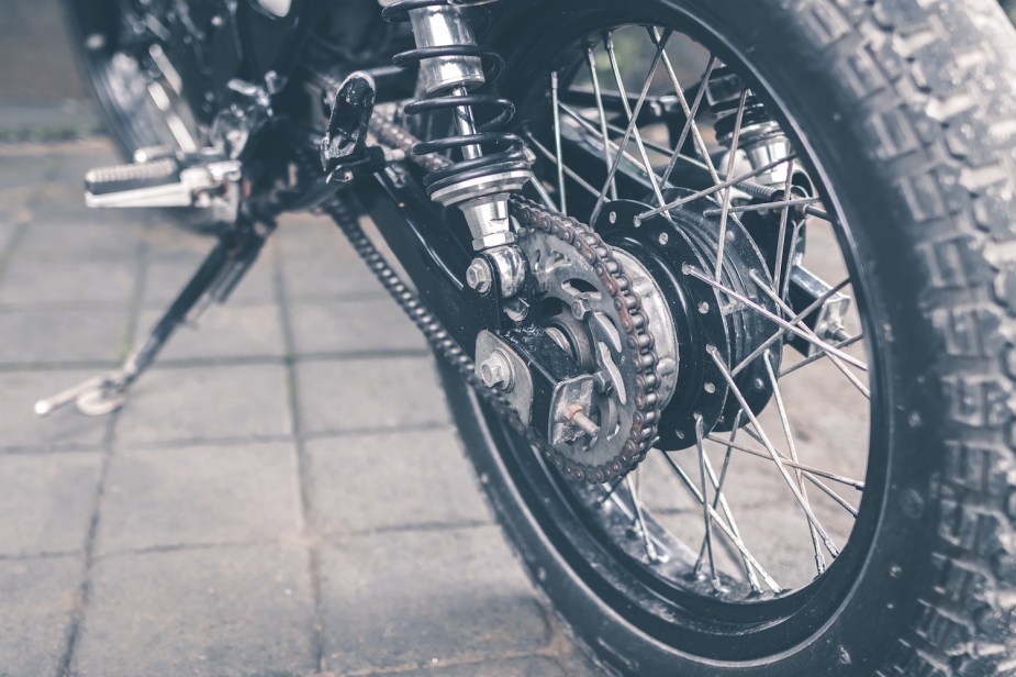 Closeup photo of a knobby, off-road motorcycle tire, flagstones visible in the distance.