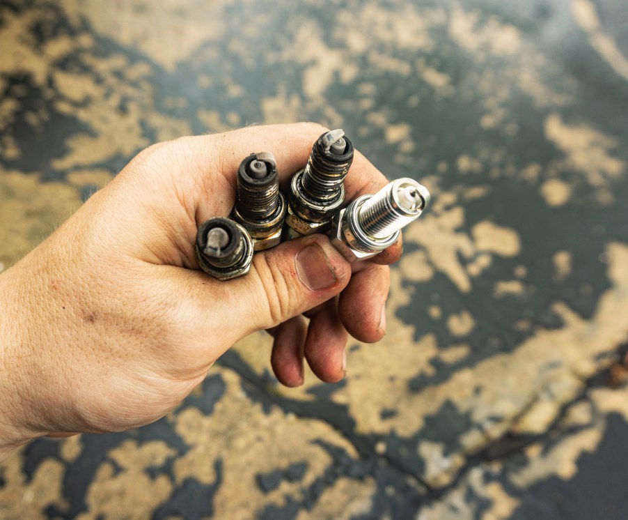 Several old and dirty 2013 Fiat 500 Abarth spark plugs next to a clean new one