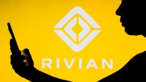 The Rivian EV company logo with a silhouette of someone on a smartphone in the foreground