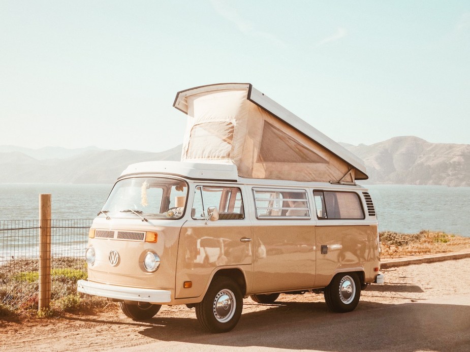 Tan Volkswagen van parked by the beach, its camper top lifted up.