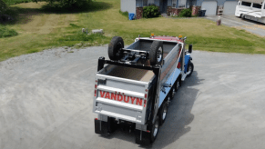 A dump truck with a rooftop drop axle and two wheels, a suburban home visible in the background.