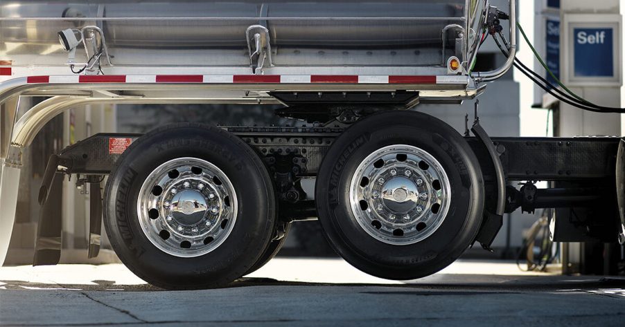 Semi truck lift/drop axle lifted off the ground, gas pumps visible in the background.