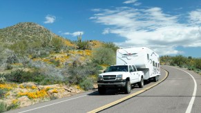 Truck towing 5th wheel camper cruises down North Lake Road at Bartlett Lake Recreation Area during the spring poppy bloom in the Tonto National Forest, Arizona.