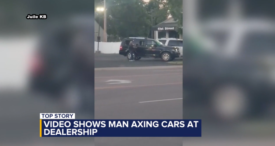 video screen shot of man hitting new cars at dealership with an axe.