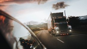 A tractor trailer driving down a country road at dusk with its amber marker lights glowing.