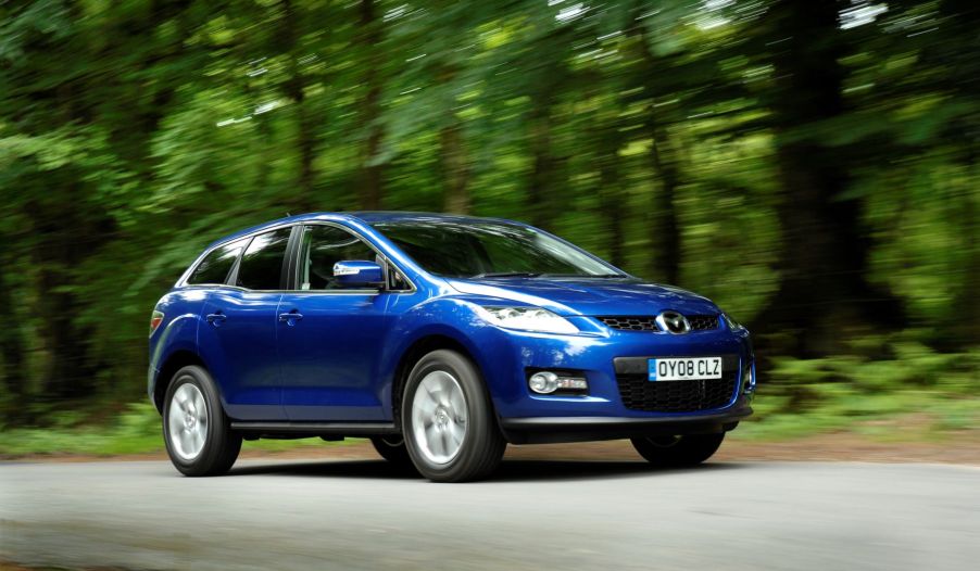 A blue 2008 Mazda CX-7 midsize crossover SUV driving on a forest road