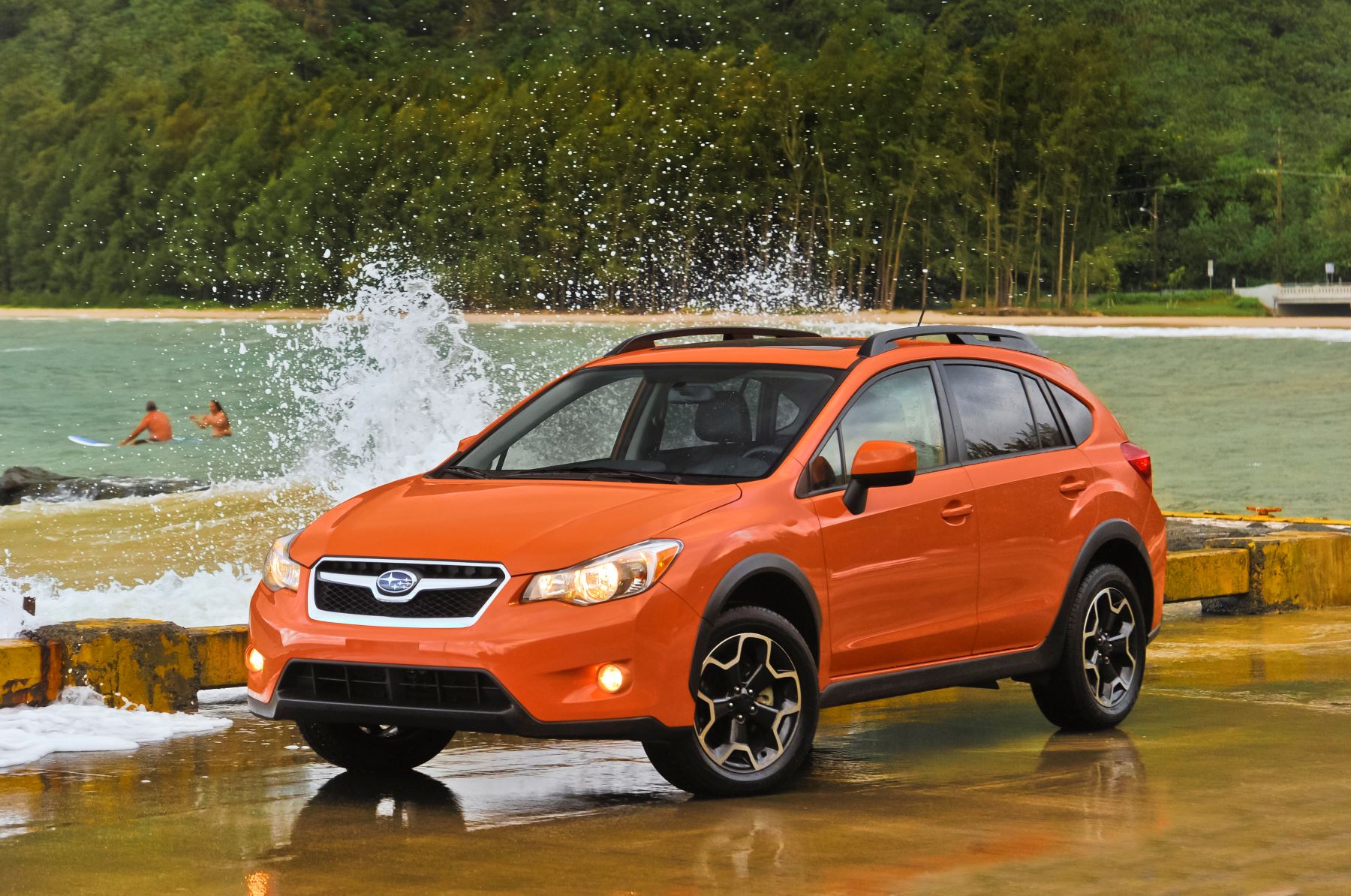 An orange 2013 Subaru XV Crosstrek compact SUV parked on a wet pier near splashing washes from a forest lake