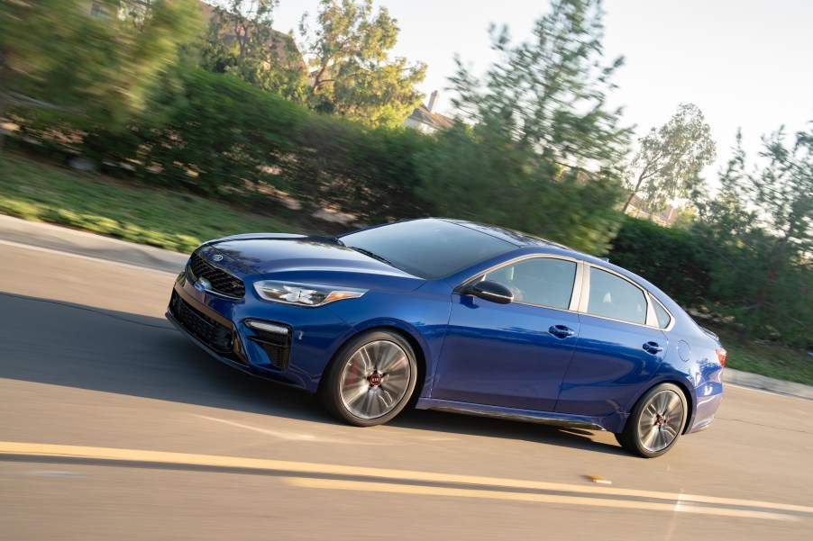 A blue 2020 Kia Forte GT driving down a treelined street