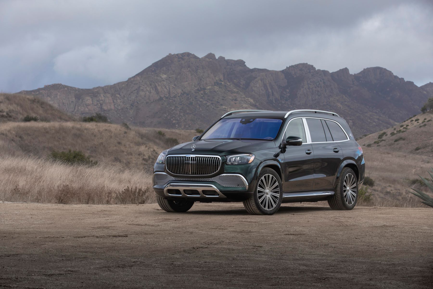 A 2021 Mercedes-Maybach GLS luxury SUV model parked on a sandy plain near rolling hills of rock and grass