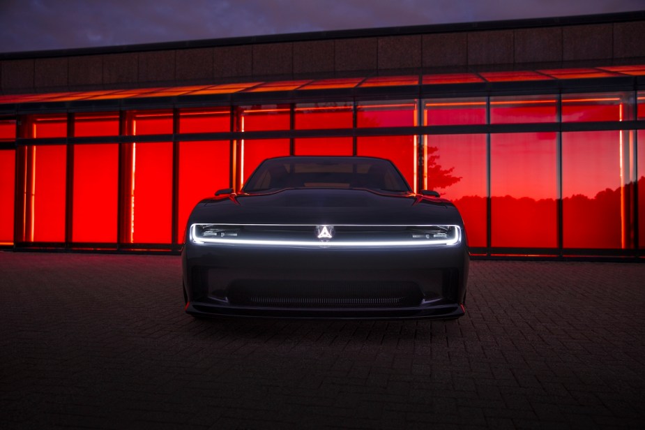 The front fascia of the Dodge Charger Daytona SRT concept EV with its illuminated Fratzog logo, a red window visible in the background.