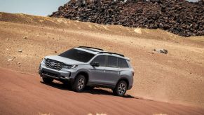 A gray 2022 Honda Passport TrailSport driving on a dirt desert dune near a large pile of garbage