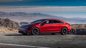 A red 2022 Mercedes-Benz AMG EQS all-electric luxury sports car sedan parked on the side of a highway road near the sea