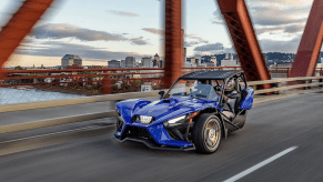 A blue Polaris Slingshot drives over a bridge.