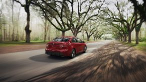 A red 2022 Toyota Corolla Hybrid drives down a back road.