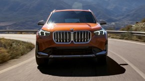 An orange 2023 BMW X1 driving down a windy road.