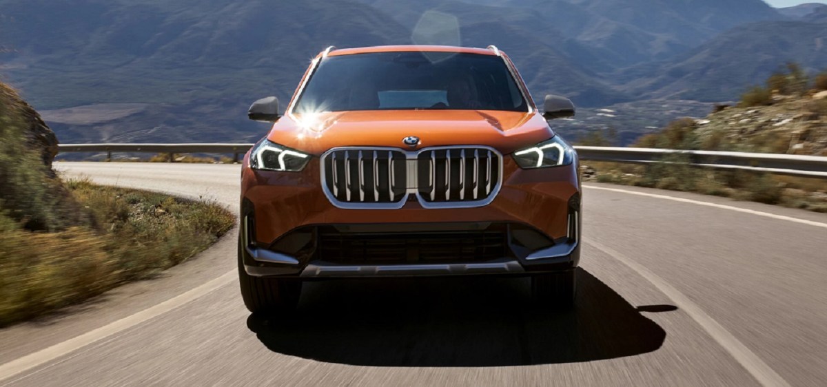 An orange 2023 BMW X1 driving down a windy road.