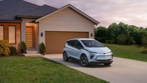 A light blue 2023 Chevy Bolt EV electric hatchback model parked on the driveway outside of a small home