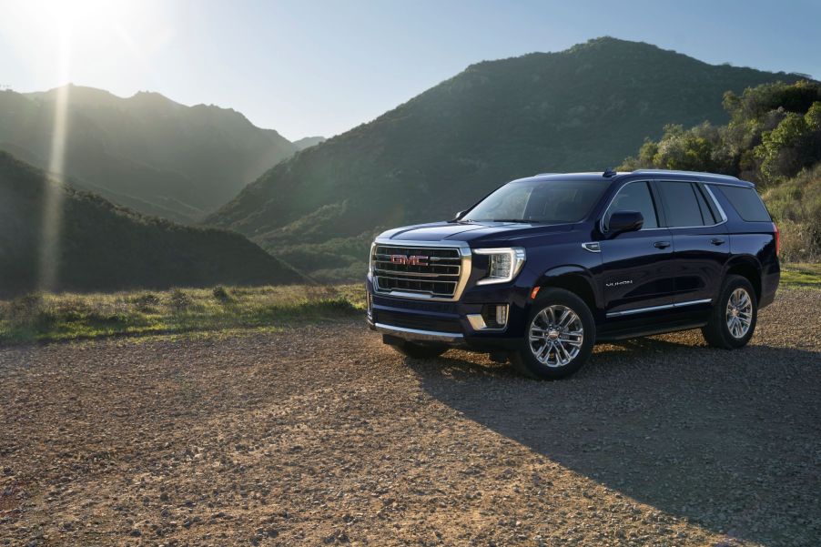 A 2023 GMC Yukon SLT full-size SUV model parked on a dirt path near grassy hills