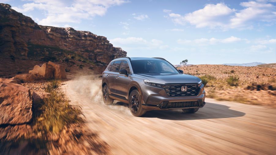 A steel gray 2023 Honda CR-V Sport hybrid compact SUV model driving on a dusty desert road