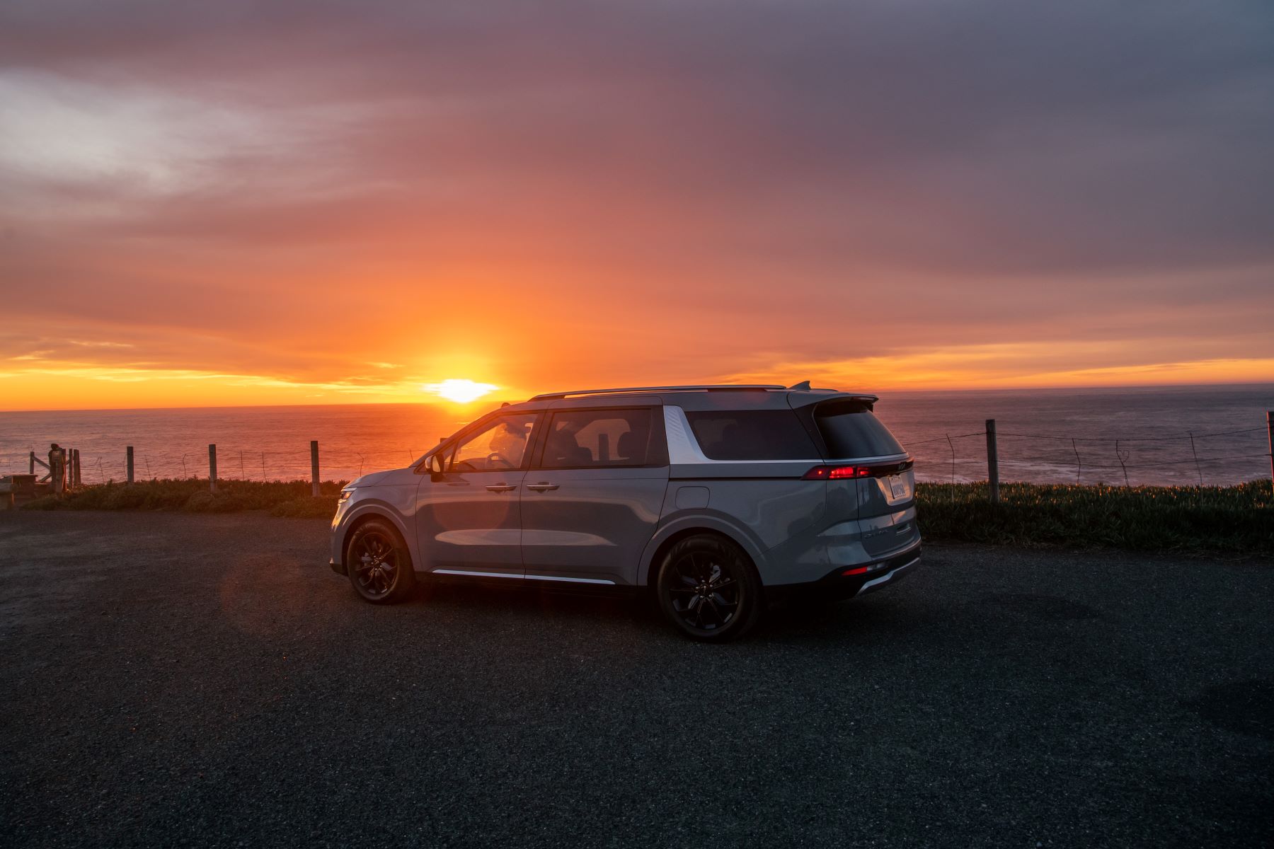 A 2023 Kia Carnival MPV/minivan parked near the water as the sunsets over the sea