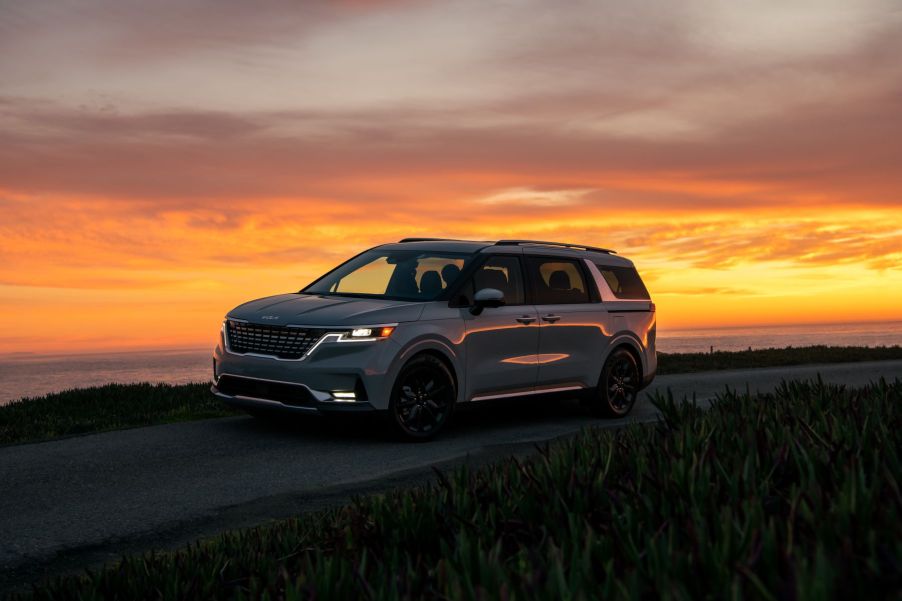 A gray 2023 Kia Carnival minivan/MPV parked on a trail near the ocean at sunset