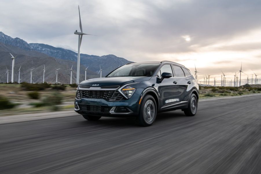 A 2023 Kia Sportage HEV (hybrid electric vehicle) compact SUV driving past a field of windmills