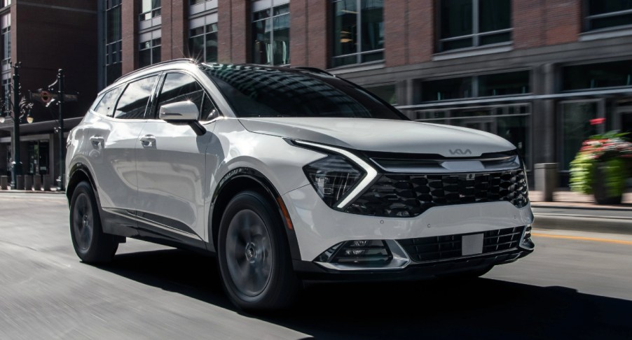 A white 2023 Kia Sportage hybrid SUV is driving on the road.