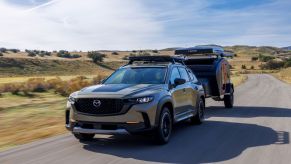 A 2023 Mazda CX-50 compact crossover SUV towing a travel trailer on a country highway