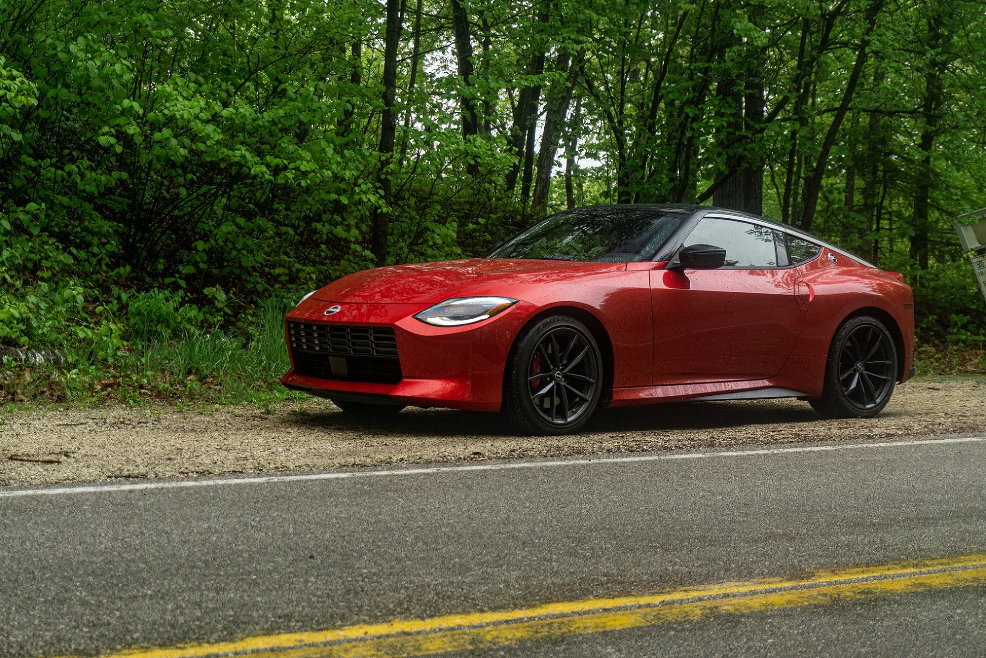 The side 3/4 view of a red 2023 Nissan Z Performance on a forest road